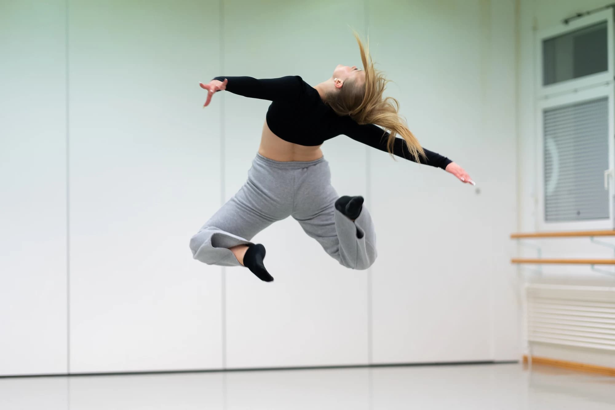 Danseuse en saut dynamique en studio de danse, bras et cheveux en mouvement – shooting photo Novacom Agency