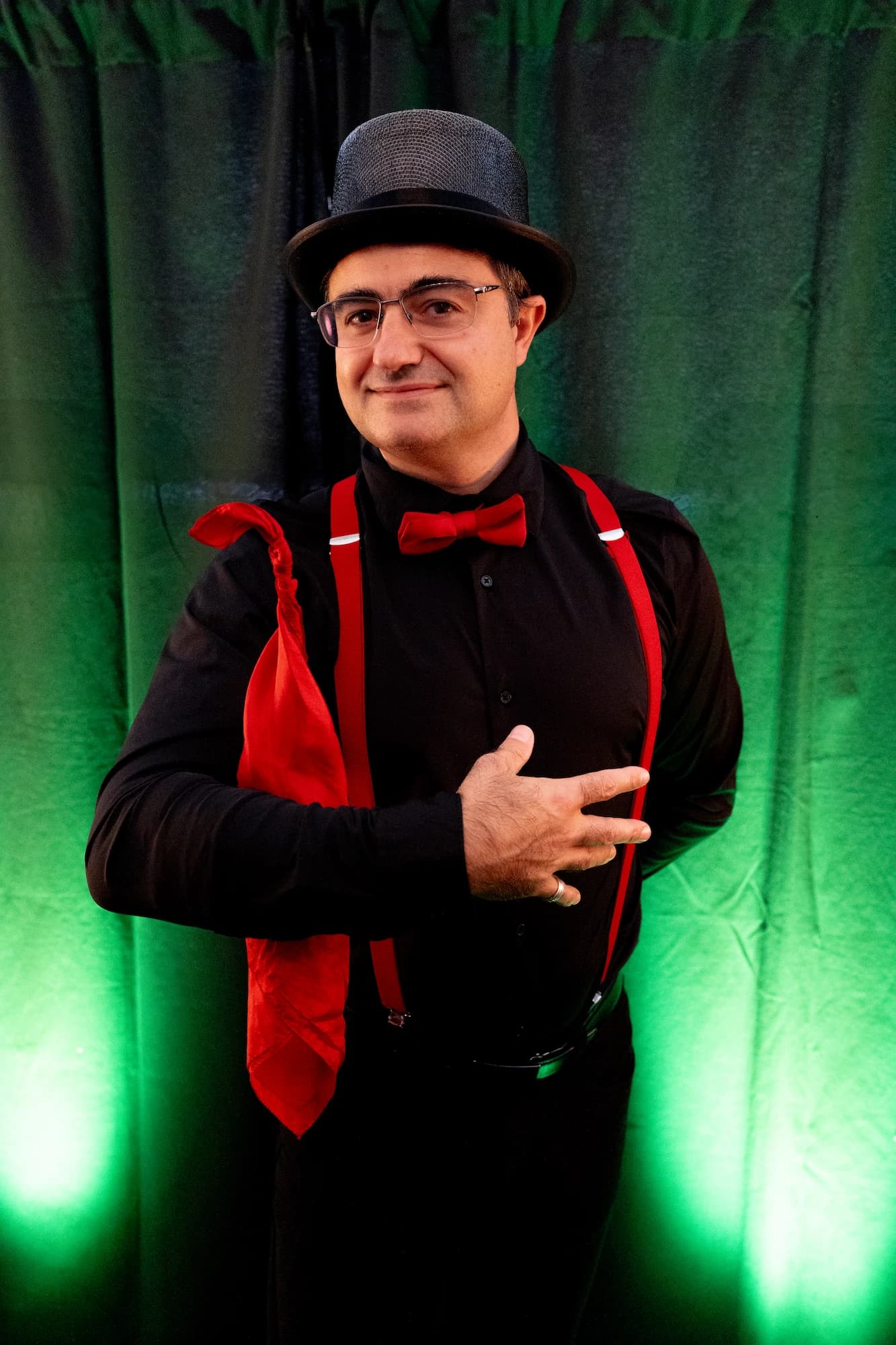 Portrait d'un magicien en costume noir, haut-de-forme et bretelles rouges sur fond vert – shooting photo Novacom Agency