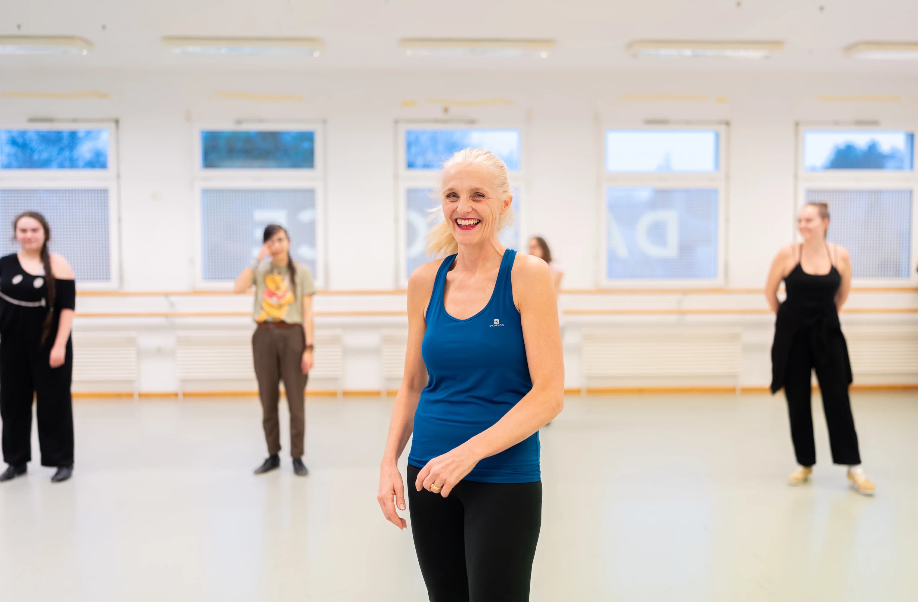 Professeure de danse souriante en studio lors d'un cours, étudiants en arrière-plan – shooting photo Novacom Agency